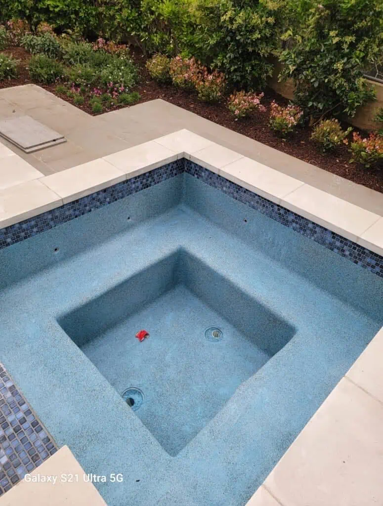 Custom spa with new pool plaster, surrounded by patio and garden landscaping.