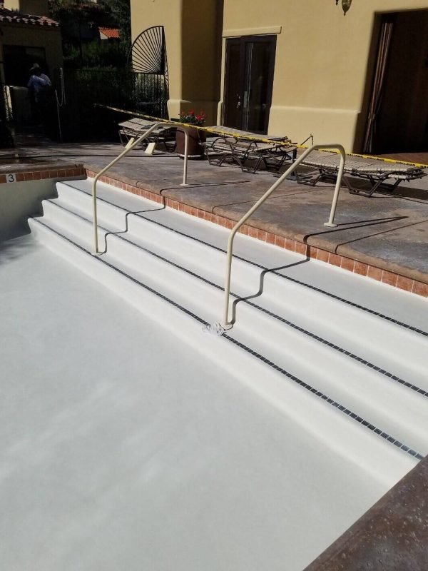 Newly resurfaced pool with smooth, white plaster finish and safety handrails.